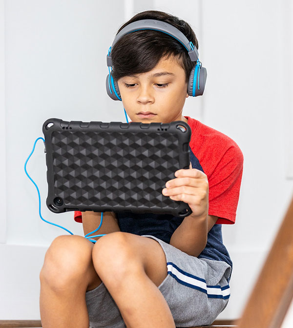 A young boy sitting on the floor with headphones on and a tablet